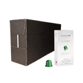 A large matte black rectangular box stands next to a small white package labeled CARRARO 1923 ALUMINIUM gran crema coffee capsules, with one green capsule placed in front on a clean white background.
